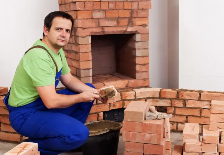 Murarz układa cegły szamotowe, budując kominek.