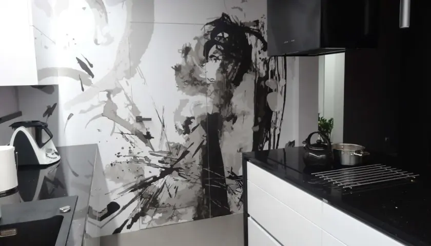 Nowoczesna kuchnia z czarnym blatem i białymi szafkami. Na ścianie artystyczny mural, który świetnie maskuje drzwi.
