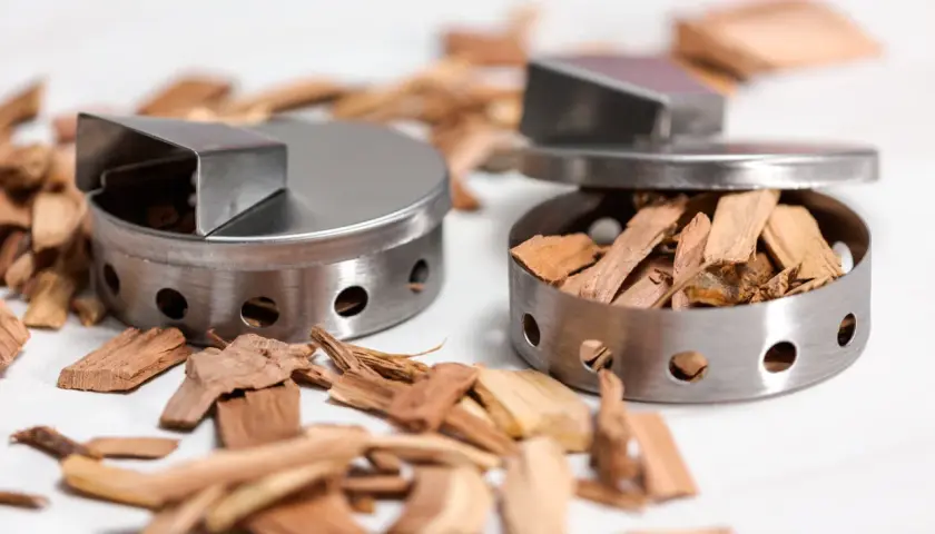 Dwa metalowe pojemniki wypełnione wiórami drzewnymi do wędzenia.