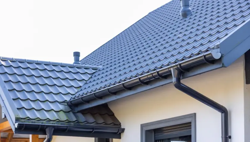 Szary dach z dachówki ceramicznej, rynny i komin. Sprawdź, jaka jest dachówka ceramiczna cena za m2.