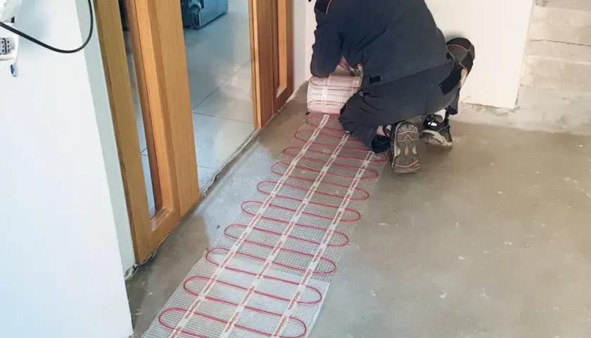 Instalator montuje matę grzewczą, przygotowując podłogę do komfortowego ogrzewania. To inwestycja w przyszłość, która obniży koszt ogrzewania podłogowego.