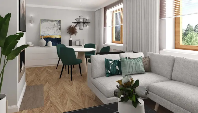 Jasnoszara kanapa z zielonymi poduszkami, okrągły stół z krzesłami w tym samym kolorze, drewniana podłoga w jodełkę i ściany w kolorze popielatym tworzą przytulne wnętrze.
