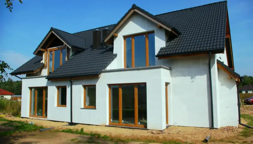 Nowy dom z białym tynkiem i ciemnym dachem, z dużymi oknami.