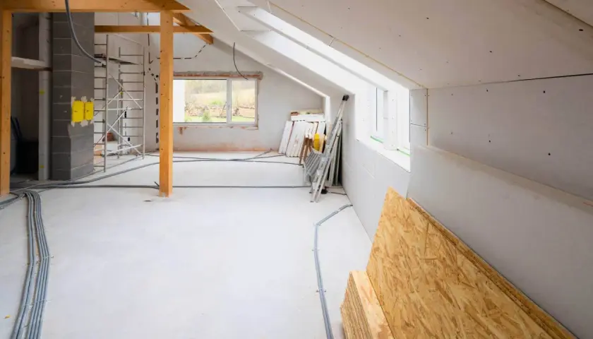 Wnętrze w trakcie rozbudowy domu. Widoczne rusztowania, materiały budowlane, instalacje elektryczne i okna.