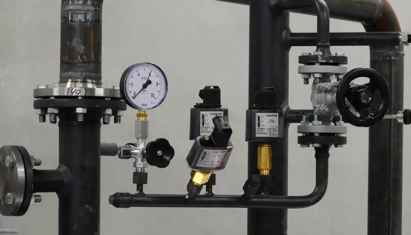 Fragment instalacji przemysłowej, prawdopodobnie w hydroforni. Widoczne rury, zawory, manometr i elektrozawory.