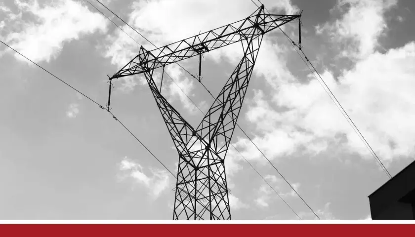 Wysoki słup energetyczny na działce, z liniami przesyłowymi na tle chmur.