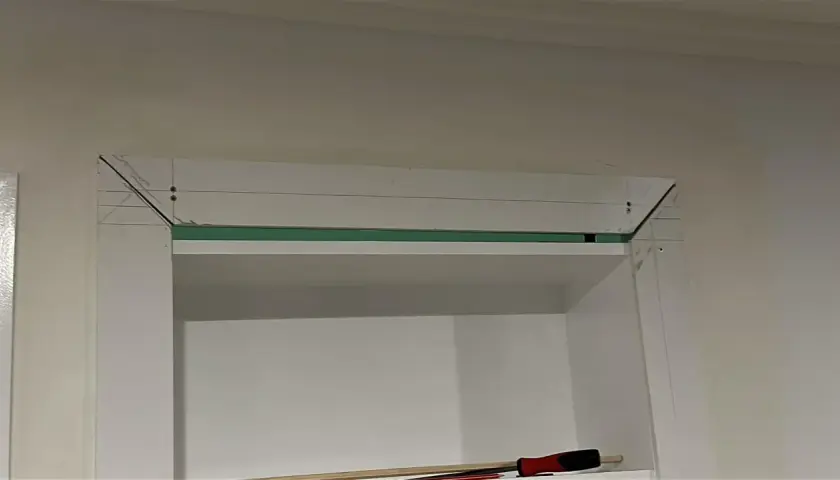 Montaż ukrytych drzwi w regale. Widoczne elementy konstrukcyjne i narzędzia.