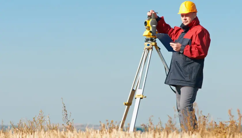 Geodeta w żółtym kasku pracuje z tachimetrem w polu. Zastanawiasz się, ile kosztuje geodeta?