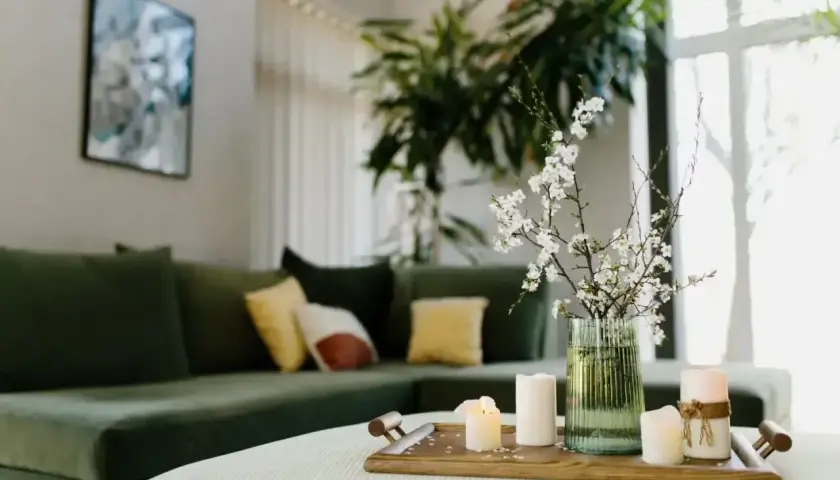 Zielona kanapa, świece i kwitnące gałązki tworzą harmonię w salonie, zgodną z zasadami feng shui.