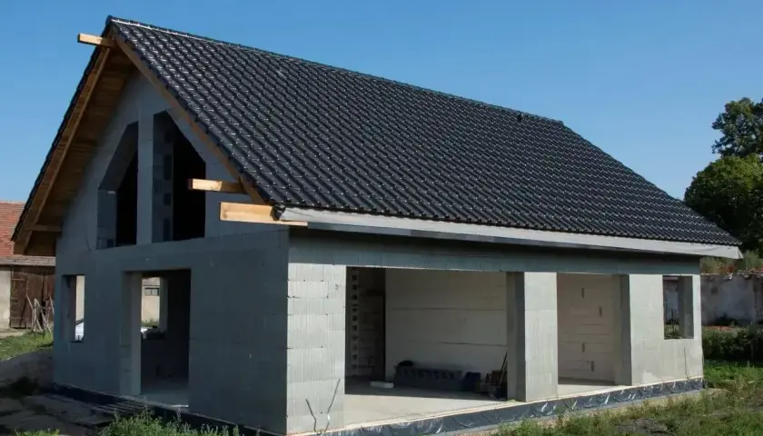 Budynek w stanie surowym otwartym, z betonowych pustaków, z dachem pokrytym czarną dachówką. Widać otwory okienne i drzwiowe.