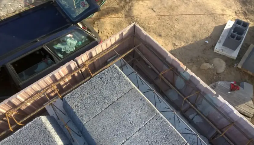 Szalowanie stropu z bloczków betonowych i zbrojenia. Obok stoi samochód.