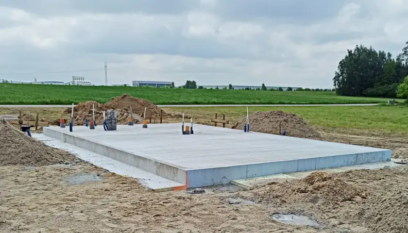 Solidny fundament z betonu, gotowy na budowę domu. Wokół piasek i zielone pola.