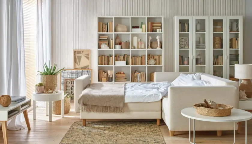 Jak pogodzić salon z sypialnią? Rozkładana sofa, regały z książkami i dekoracje tworzą przytulną przestrzeń.