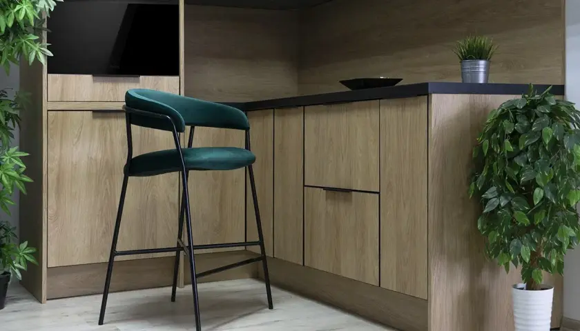 Nowoczesny blat z hokerami w kuchni. Drewniane fronty szafek i zielony, aksamitny hoker tworzą stylowe wnętrze.