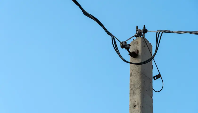 Stary słup na działce ponad 30 lat, z kablami elektrycznymi na tle błękitnego nieba.