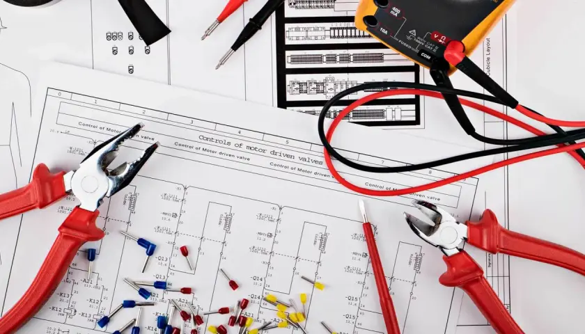 Narzędzia i schematy do elektryki w domu: kombinerki, multimetr i okablowanie na tle planów instalacji.