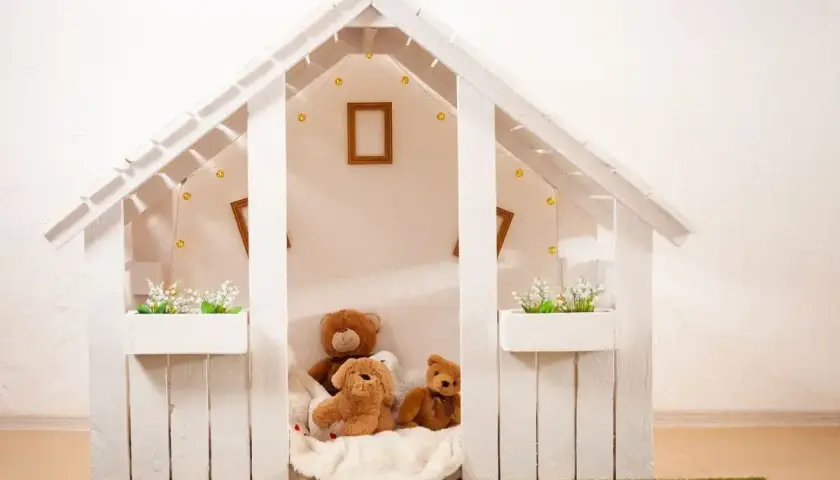 Jak zbudować domek dla dzieci? Biały, drewniany domek z pluszakami i lampkami, idealny do zabawy.