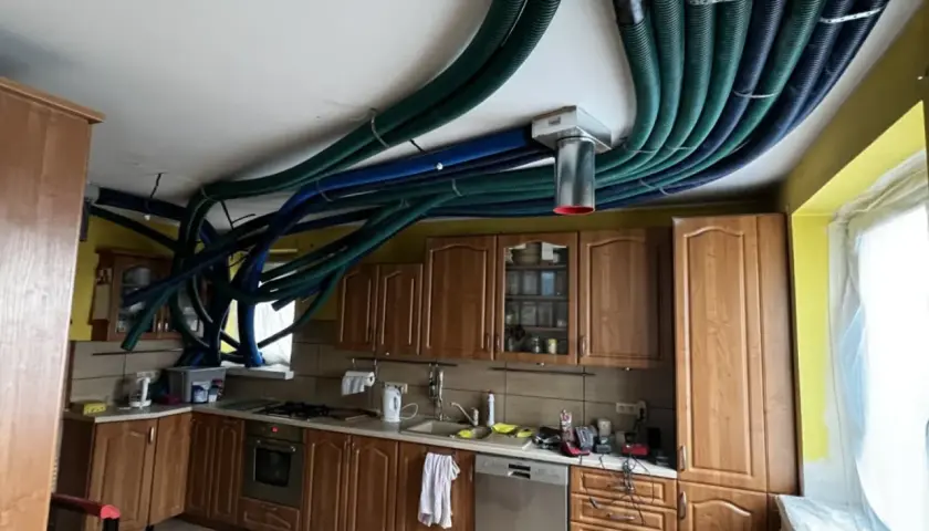 Instalacja rekuperacji w starym domu. W kuchni na suficie widać gęsto ułożone, zielone i niebieskie przewody wentylacyjne.