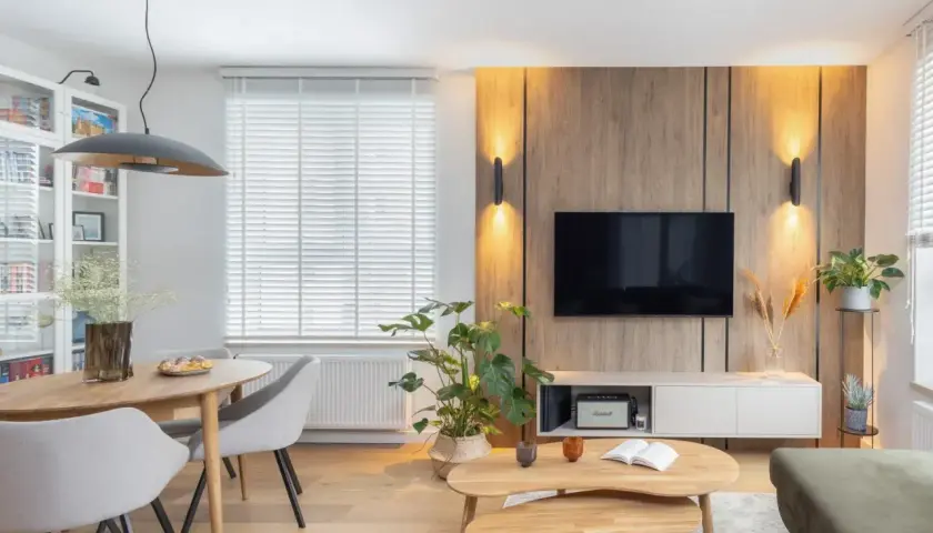 Przytulny salon inspiracje: drewniana ściana z TV, jadalnia, rośliny i wygodna sofa tworzą ciepłą atmosferę.