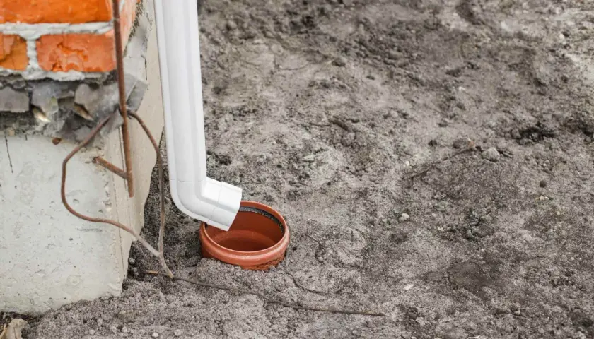 Biała rura spustowa odprowadza wodę z rynien do gruntu, do ceramicznej studzienki.