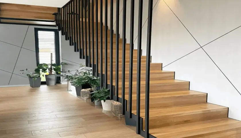 Nowoczesne drewniane schody z czarną balustradą. Zastanawiasz się, ile kosztuje zrobienie schodów? Warto rozważyć ten projekt.