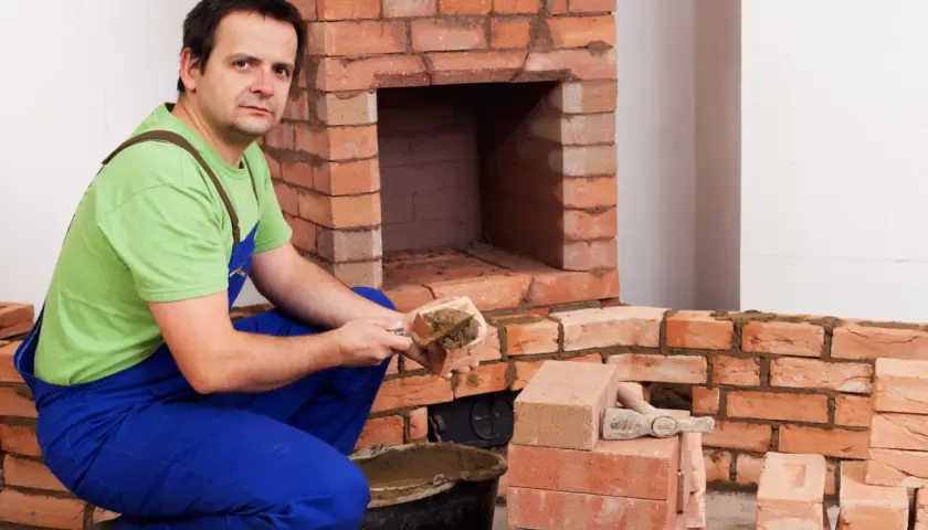 Murarz układa cegły szamotowe, budując kominek.