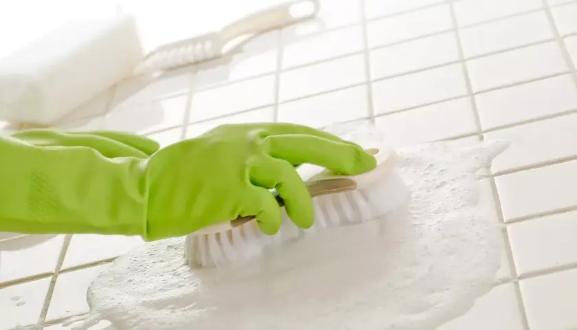 Ręka w zielonej rękawiczce szoruje szczotką białe fugi pokryte pianą.