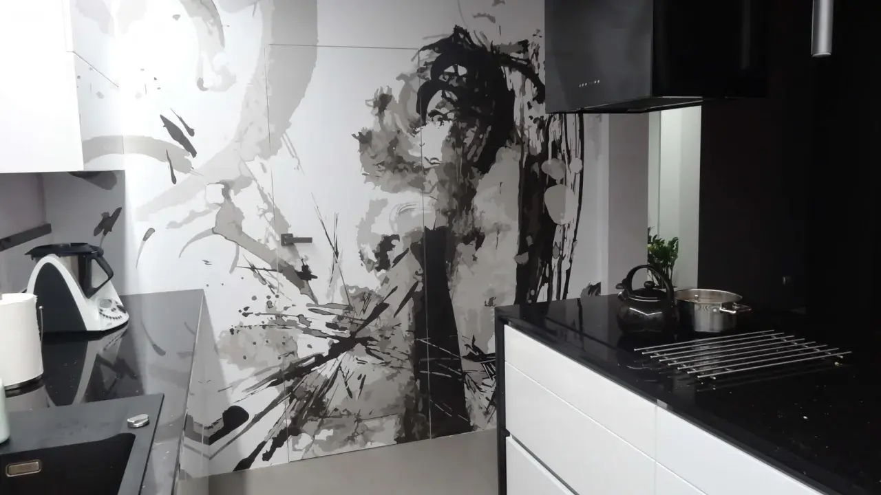 Nowoczesna kuchnia z czarnym blatem i białymi szafkami. Na ścianie artystyczny mural, który świetnie maskuje drzwi.