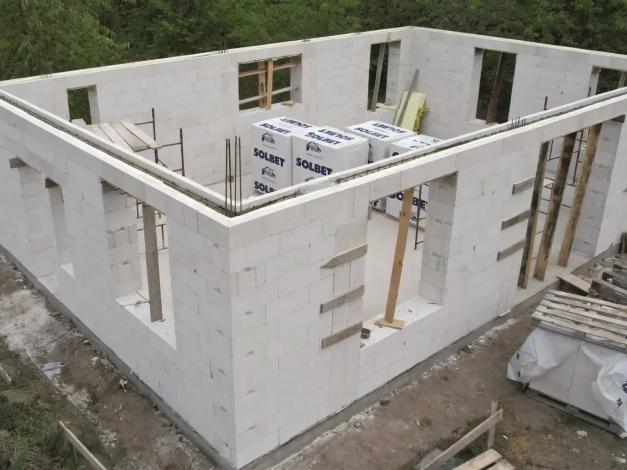 Budowa domu z bloczków z betonu komórkowego. Widoczne ściany z otworami okiennymi i drzwiowymi, materiały budowlane.