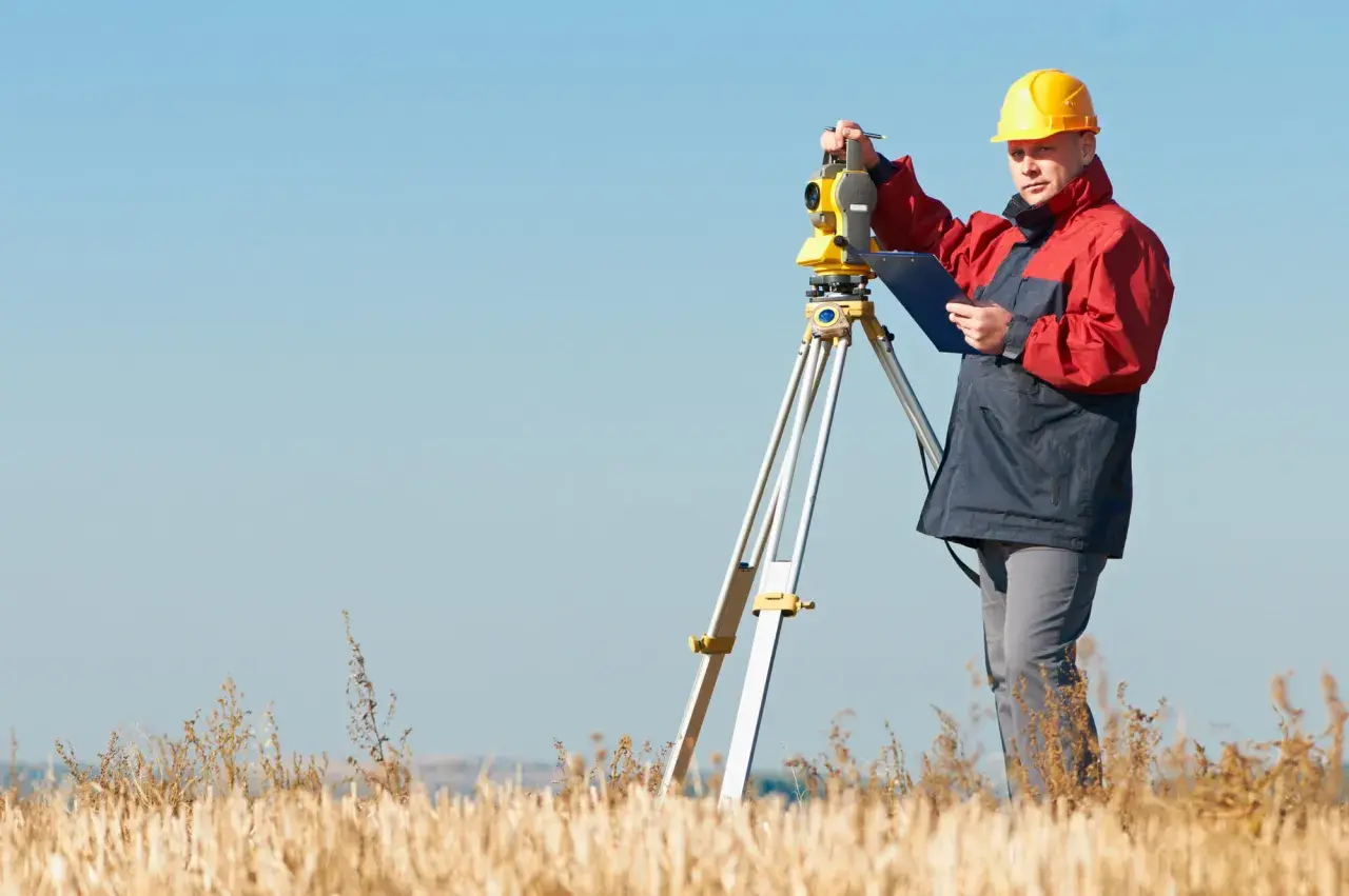Geodeta w żółtym kasku pracuje z tachimetrem w polu. Zastanawiasz się, ile kosztuje geodeta?