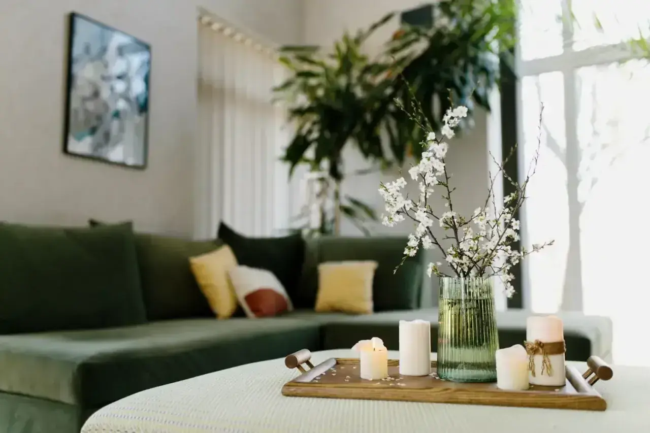 Zielona kanapa, świece i kwitnące gałązki tworzą harmonię w salonie, zgodną z zasadami feng shui.