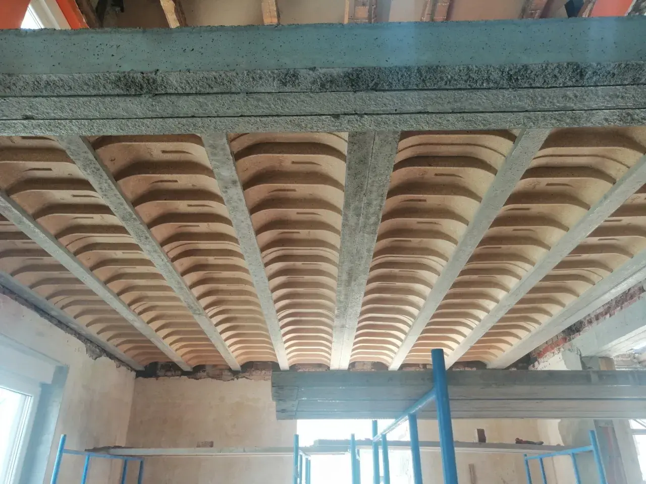 Widok od dołu na betonowe belki stropowe i pustaki ceramiczne, tworzące przestrzeń przypominającą sufit katedralny.