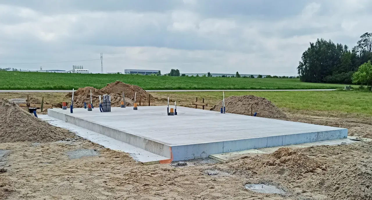 Solidny fundament z betonu, gotowy na budowę domu. Wokół piasek i zielone pola.