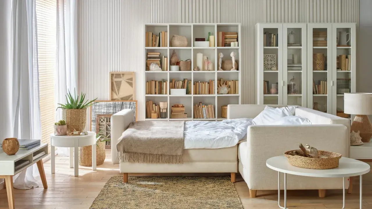 Jak pogodzić salon z sypialnią? Rozkładana sofa, regały z książkami i dekoracje tworzą przytulną przestrzeń.