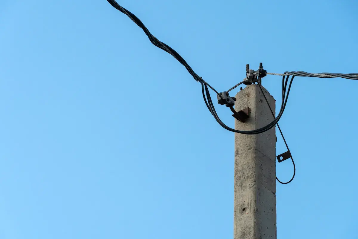 Stary słup na działce ponad 30 lat, z kablami elektrycznymi na tle błękitnego nieba.