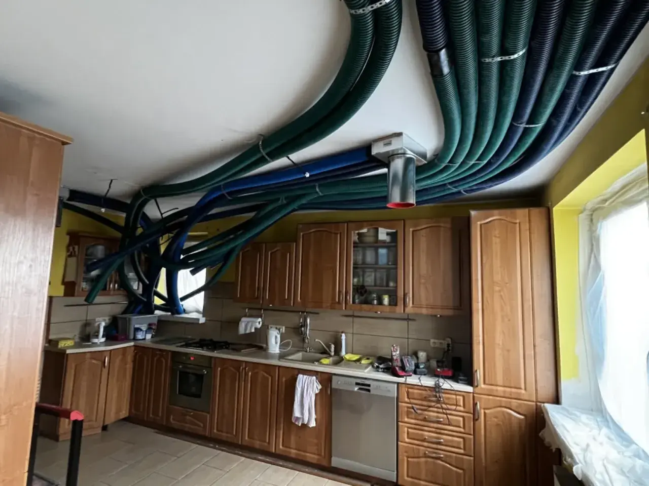 Instalacja rekuperacji w starym domu. W kuchni na suficie widać gęsto ułożone, zielone i niebieskie przewody wentylacyjne.