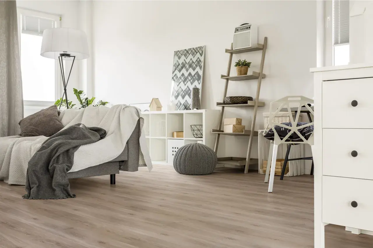 Jasne, oto propozycja:

Nowoczesny salon z szarą kanapą i kocami, białą komodą i regałem. Podłoga wygląda jak panele laminowane czy winylowe.