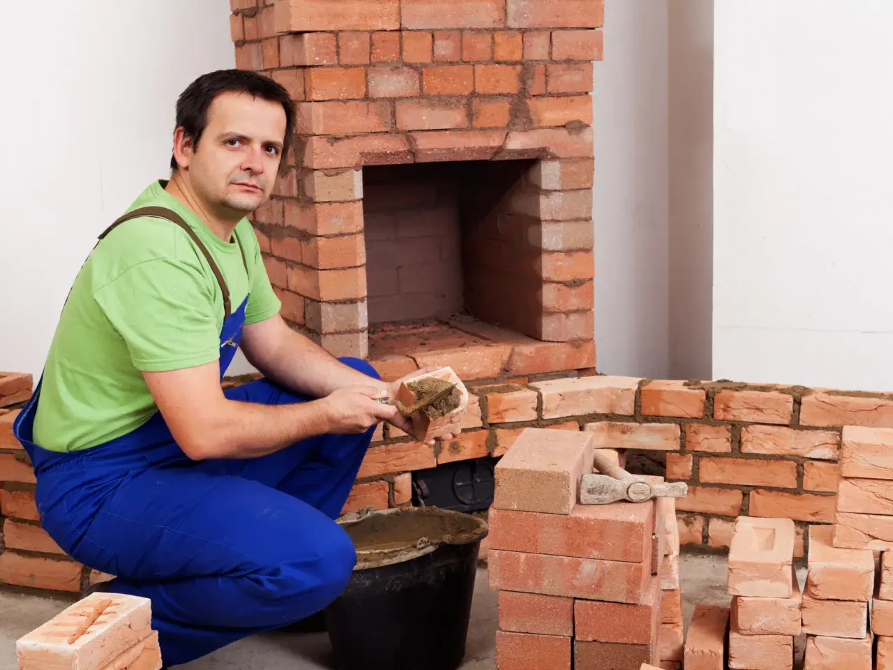Murarz układa cegły szamotowe, budując kominek.