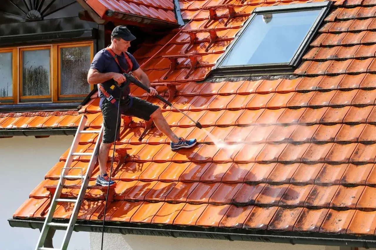 Mężczyzna na drabinie myje dach myjką ciśnieniową. Sprawdź, jaka jest mycie dachu cena i odśwież wygląd swojego domu!