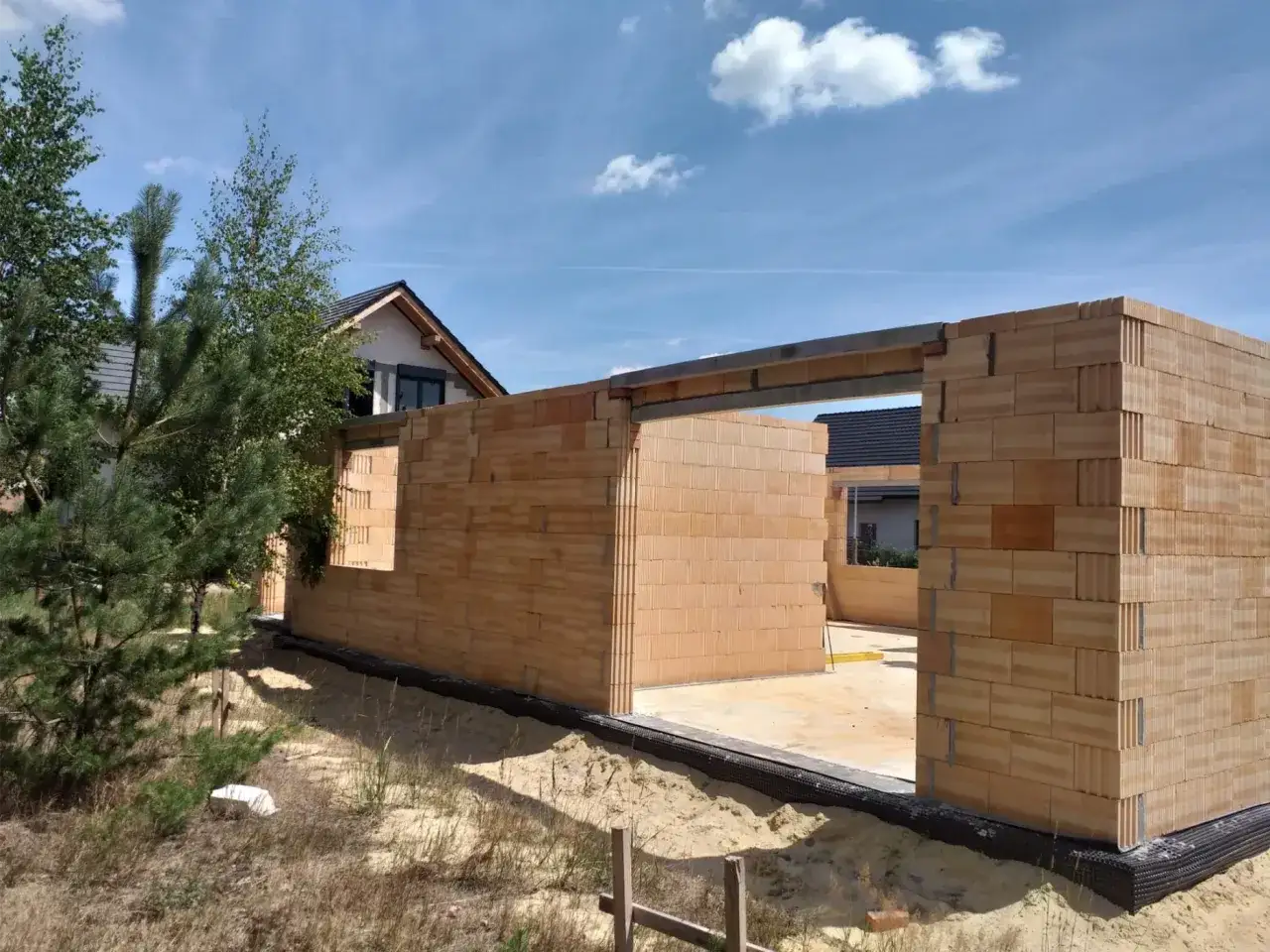 Budowa domu krok po kroku: wznoszone ściany z pustaków ceramicznych, w tle dom z dachem.