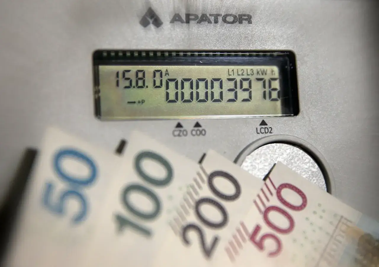 Licznik energii elektrycznej z wyświetlaczem pokazuje zużycie prądu. Obok leżą banknoty 50, 100, 200 i 500 zł, sugerując rachunki za prąd w taryfie G12W Tauron.