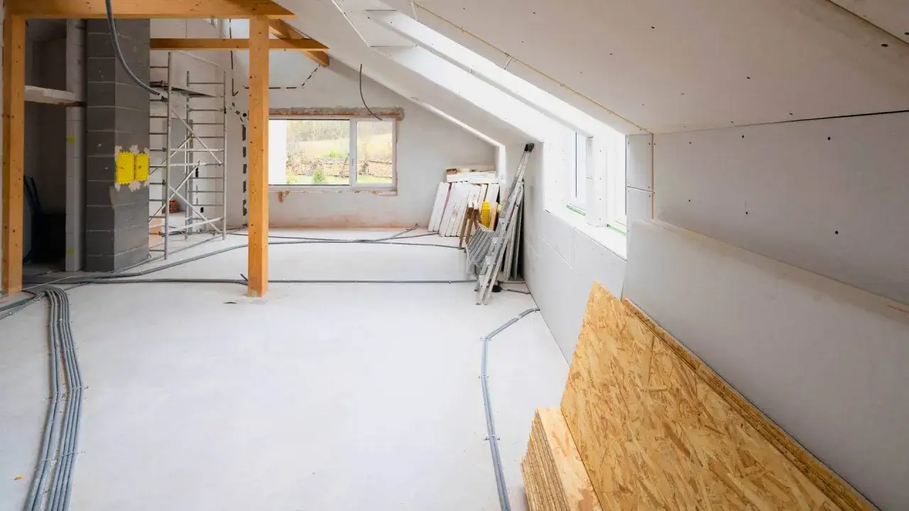Wnętrze w trakcie rozbudowy domu. Widoczne rusztowania, materiały budowlane, instalacje elektryczne i okna.