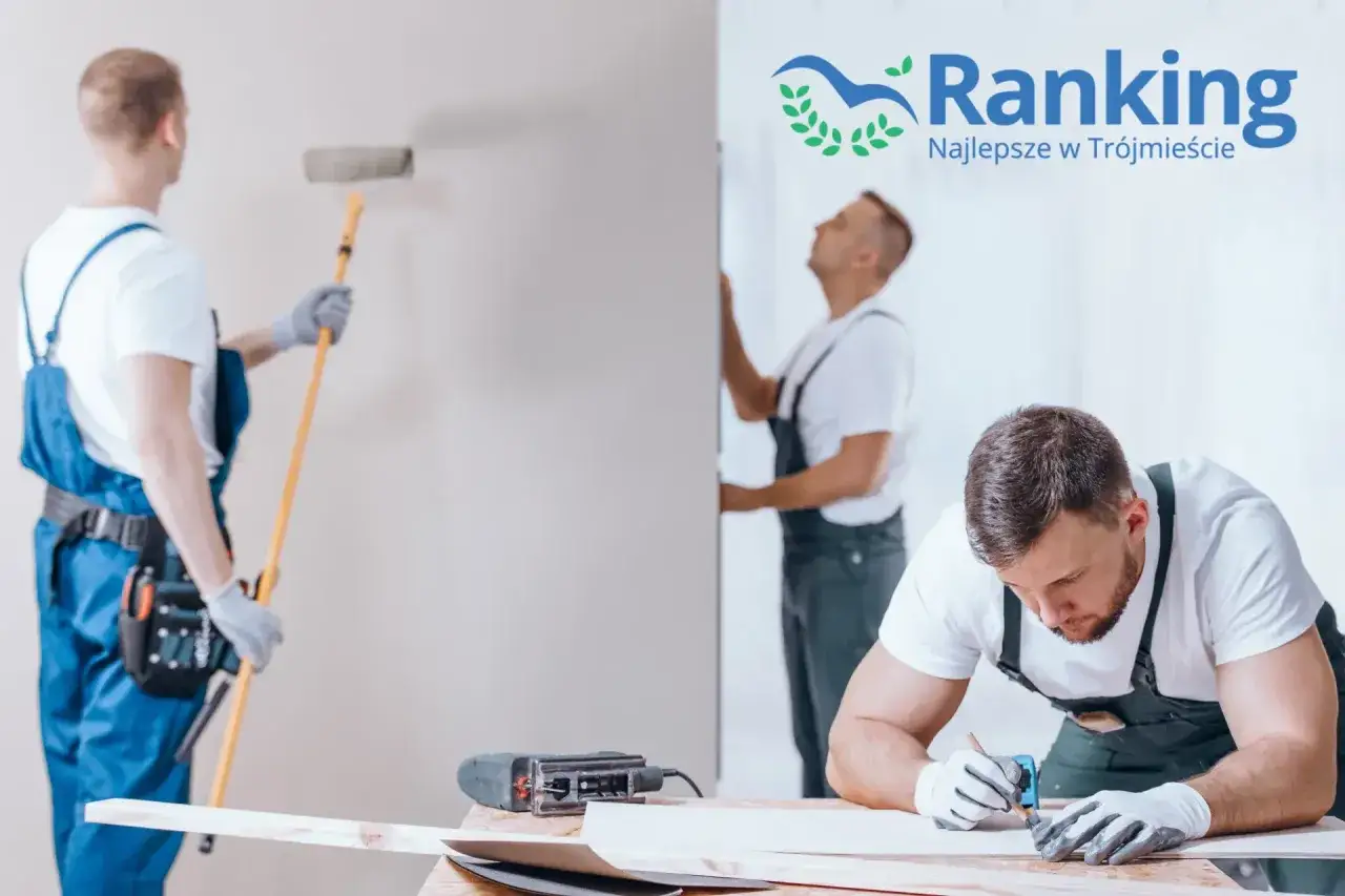 Trzech budowlańców w kombinezonach wykonuje prace remontowe. Jeden maluje ścianę wałkiem, drugi przycina płytę, trzeci mierzy.