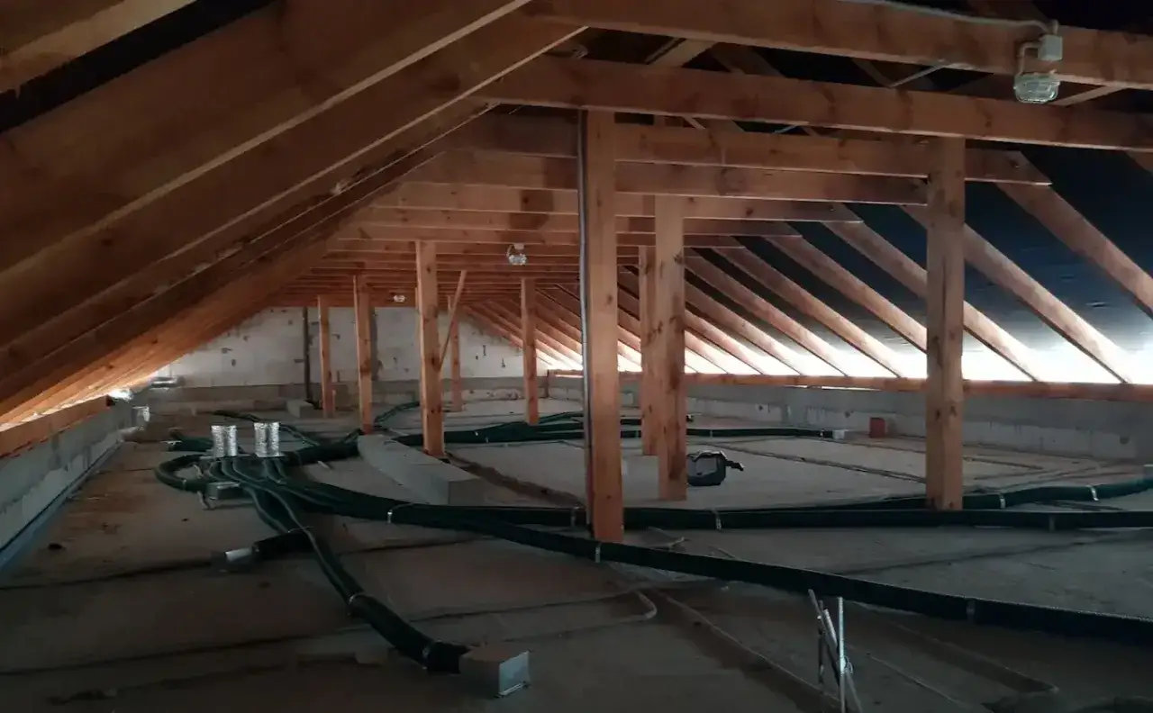 Instalacja rekuperacji w starym domu, widok na poddasze z drewnianą więźbą dachową i zielonymi przewodami wentylacyjnymi.