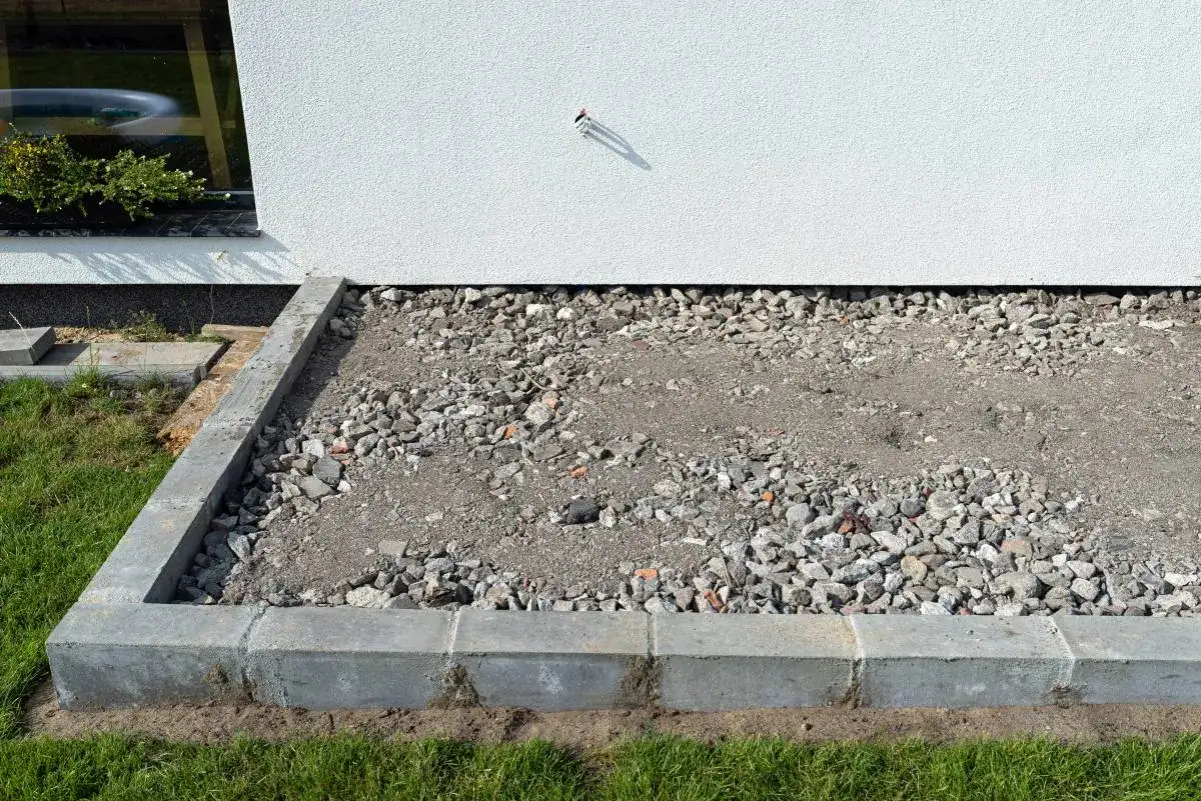 Teren wokół domu z żwirem i betonowymi krawężnikami. To najtańsza opaska wokół domu, która chroni fundamenty przed wilgociącią.