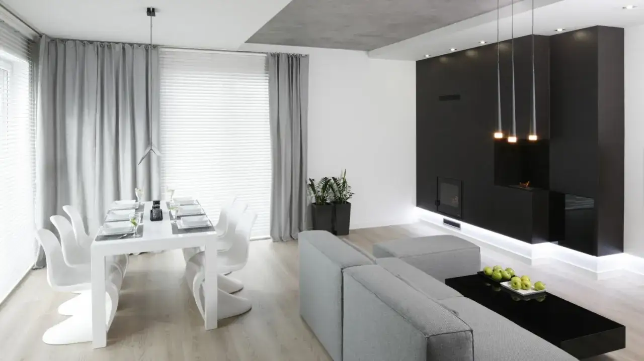 Nowoczesny salon z jadalnią. Czarny biokominek grzeje, a obok stoi szara kanapa i czarna ława z jabłkami.